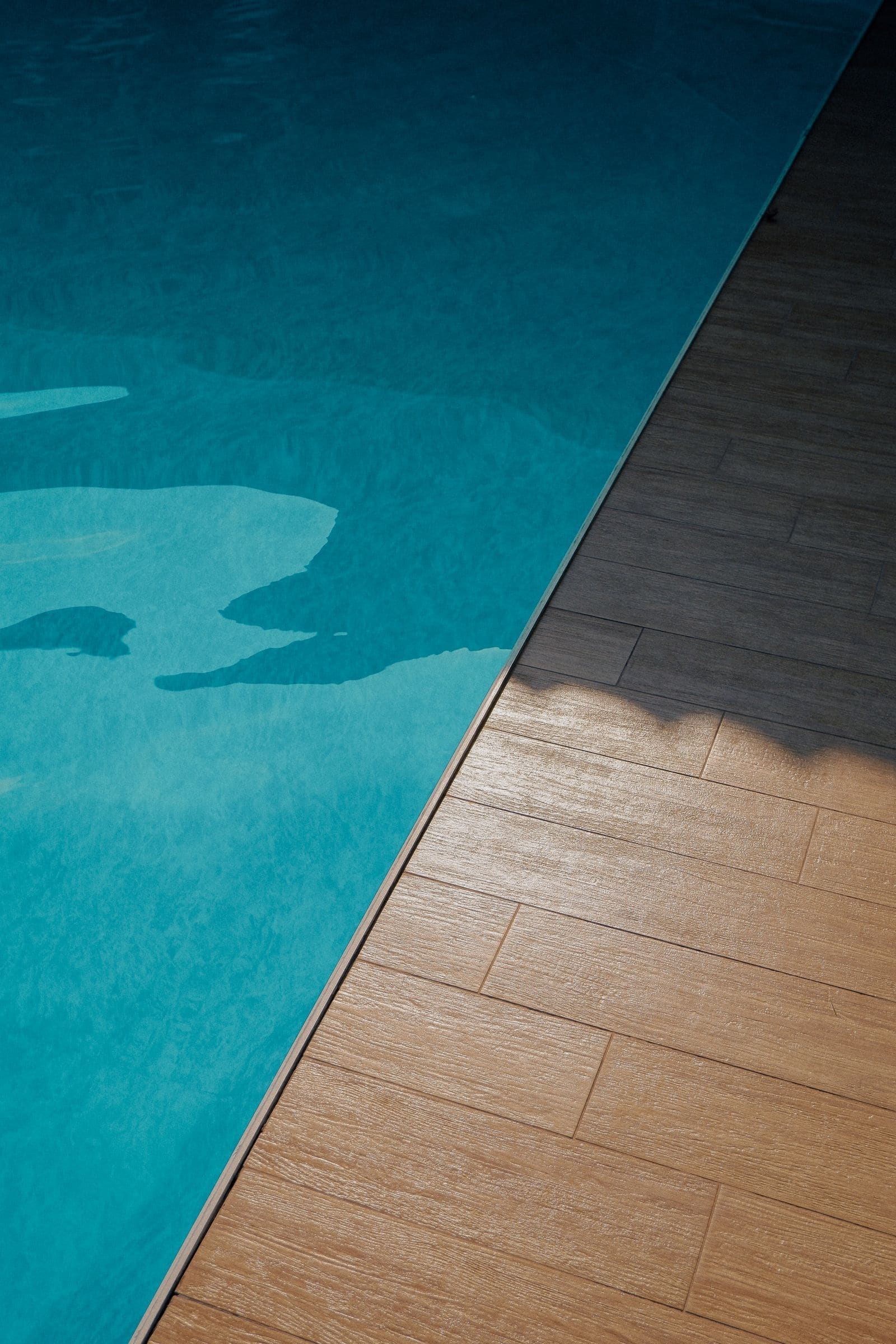 Edge of a pool meeting a wood-look deck in afternoon light