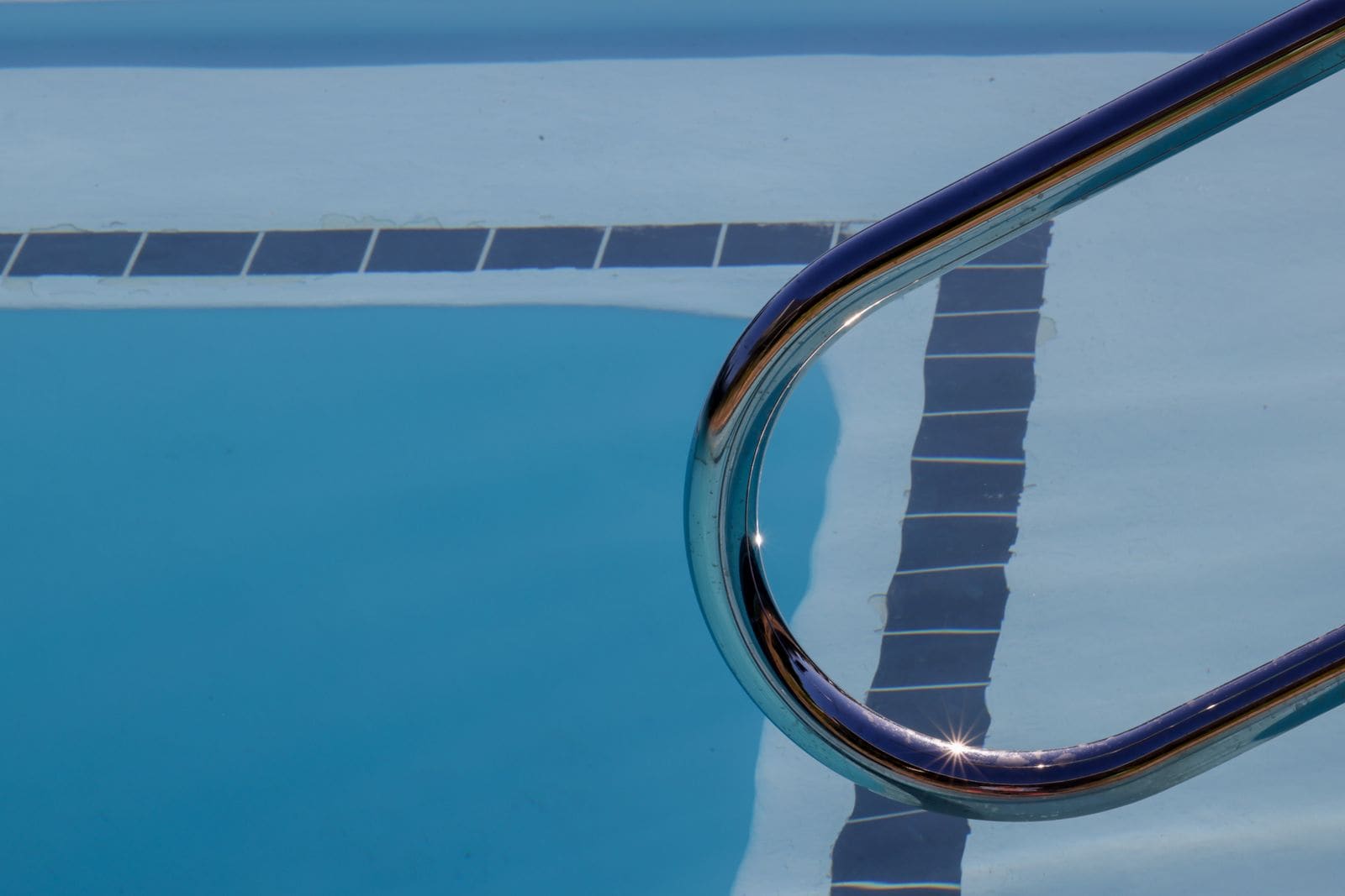 Close-up of a polished steel pool ladder rail beside blue pool tile