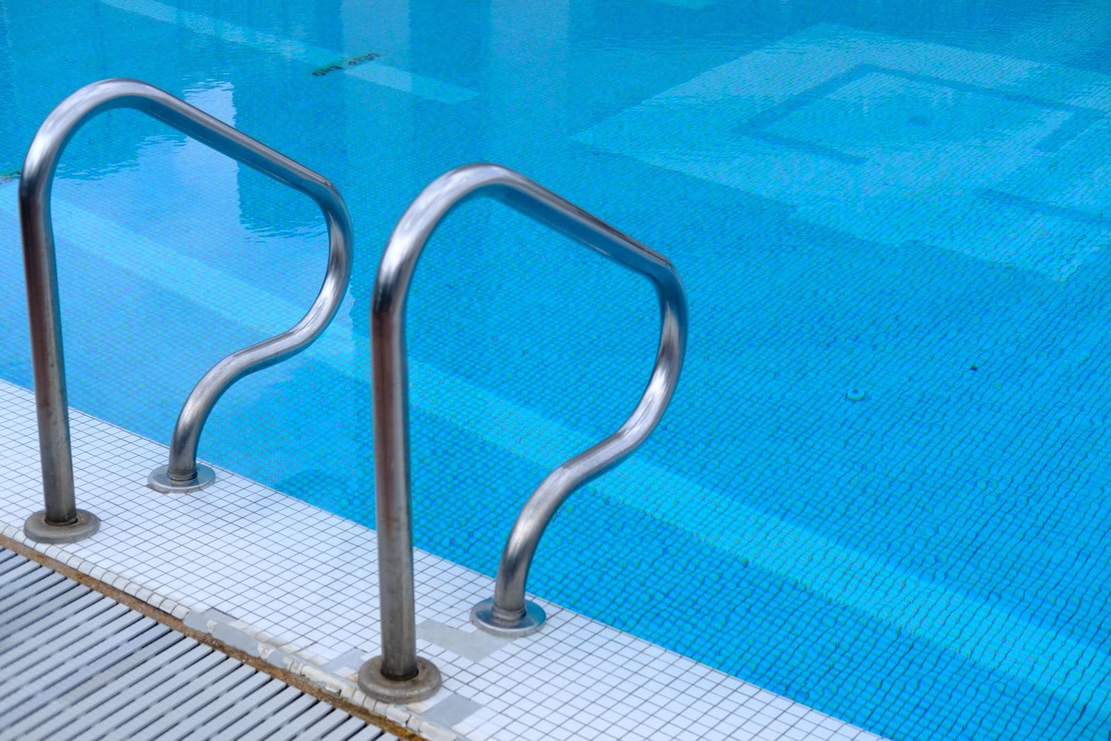 Two stainless steel pool ladder rails beside a tiled pool